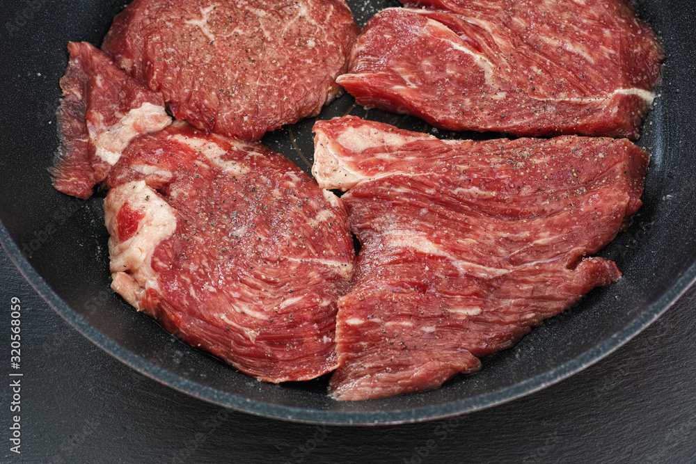 Fresh raw beef in a pan with black pepper and sea salt