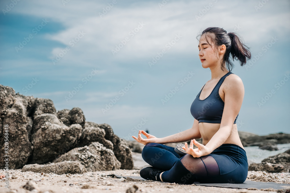 Young Asian woman practicing yoga exercise at quiet rock pier with sea background. Sport and recreation in city rush.