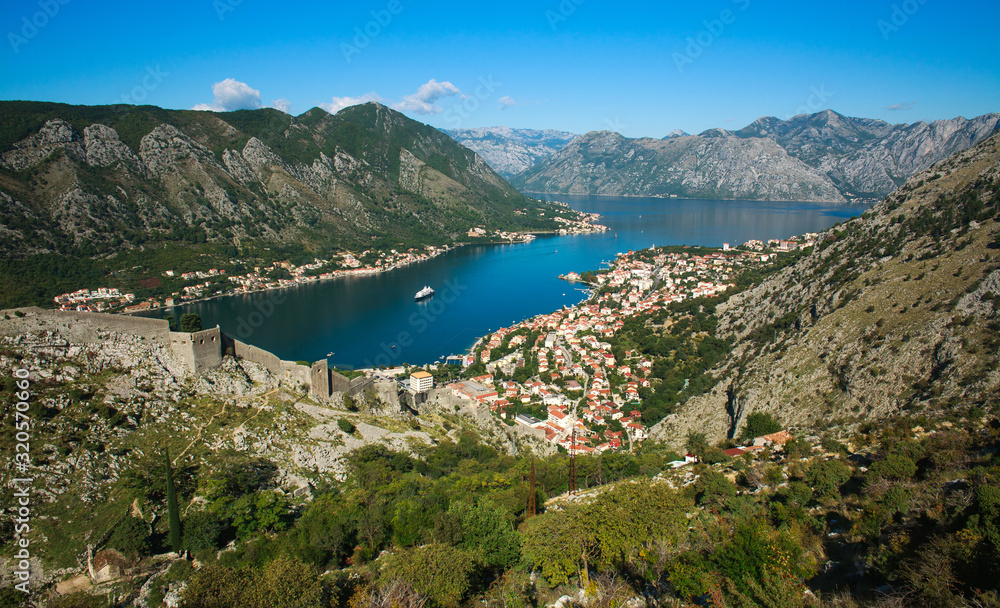 Top view of Kotor bay and old town surrounded by rocks of mountains on blue sky
