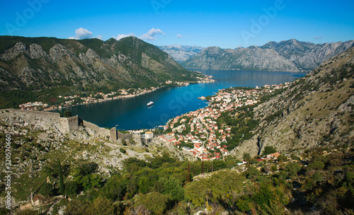 Top view of Kotor bay and old town surrounded by rocks of mountains on blue sky