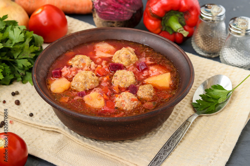 Soup with meatballs and vegetables in a dark bowl