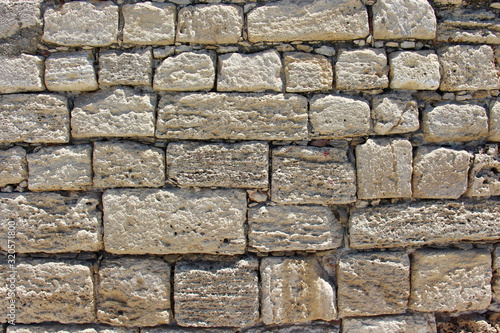 background of a solid stone wall made of cement, limestone and light rectangular bricks with an uneven surface of different colors and compositions