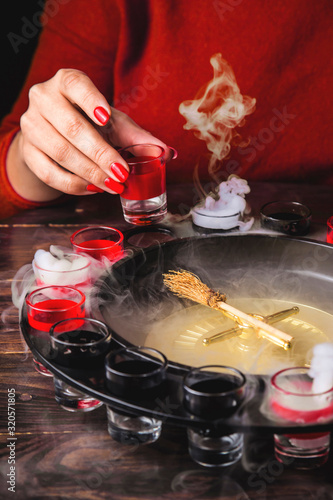 Alcoholic roulette game with wineglasses and a witch's broom instead of a pointer. Woman holds a drink. Among the white smoke. photo