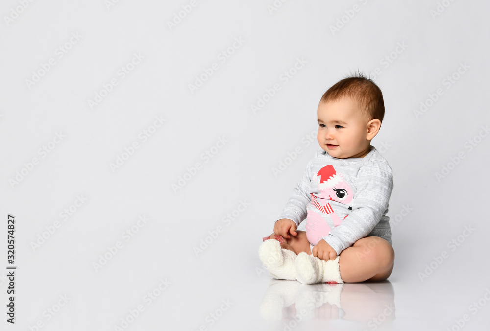 Little kid in socks and bodysuit with christmas flamingo print. She sitting on the floor isolated on white. Close up, copy space Little kid in socks and bodysuit with christmas flamingo print. She sitting on the floor isolated on white. Close up, copy space