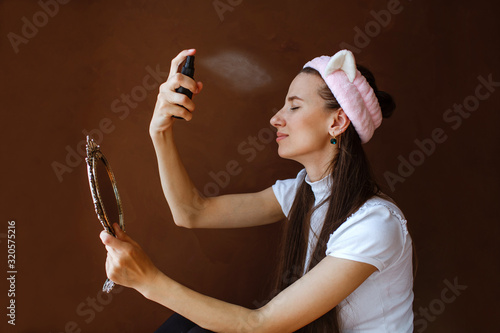 Beautiful brunette fixes her makeup with a spray for the face.