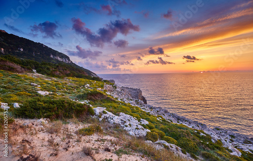 Amazing sunset view with multicolored clouds. Incredibly romantic sunrise on Voidokilia beach, Ionian Sea, Pilos town location, Greece, Europe. View of the ocean through the rocky shore.