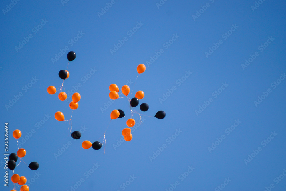 A lot of black and orange balloons on a blue sky.