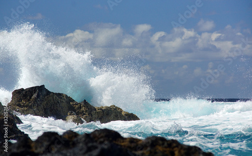 Big waves beating against rock shore of Sao Miguel island, Azores. Water splash, background of blue ocean, cloudy sky