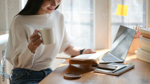 A picture of a young student holding a cup of coffee and reading in a beautiful light cafe.