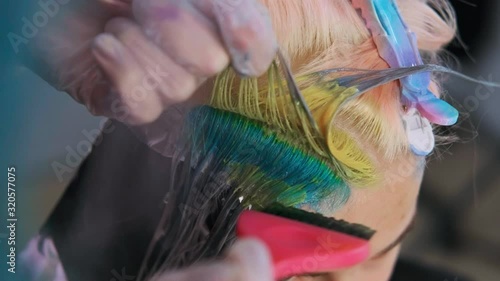 Hairdresser colorist puts paint on the hair with a brush. A short haircut, shaved temple, ornament on the hair. Coloured hair dye in the salon.