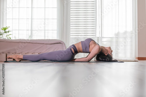 Beautiful Attractive Asian woman practice yoga Fish or yoga Matsyasana pose to meditation with yoga in bedroom,Recreation in holidays concept