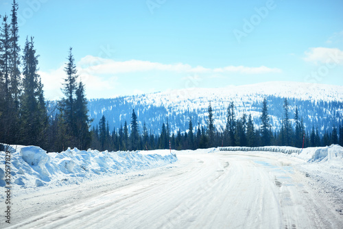 A view of the empty road through the coniferous forest. Snow-covered mountains in the background. Winter landscape. Kola Peninsula, Murmansk region, Polar Circle, Karelia, Russia photo