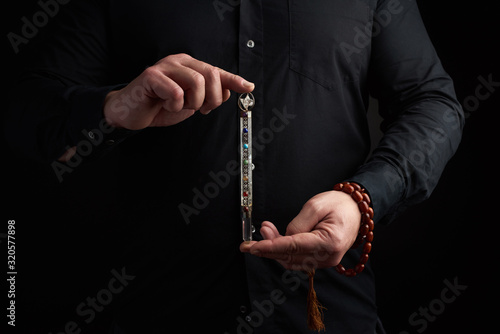 adult man in a black shirt holds a crystal chakra rod inlaid with semiprecious stones