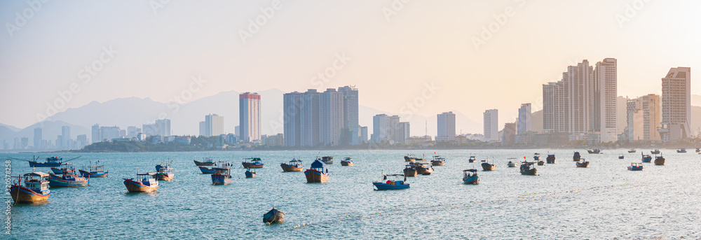 Nha Trang city panorama, famous tourism destination in Vietnam for russian expats. Nha Trang bay with boats floating on ocean. Sunset light beyond skyscrapers hotels on beach.