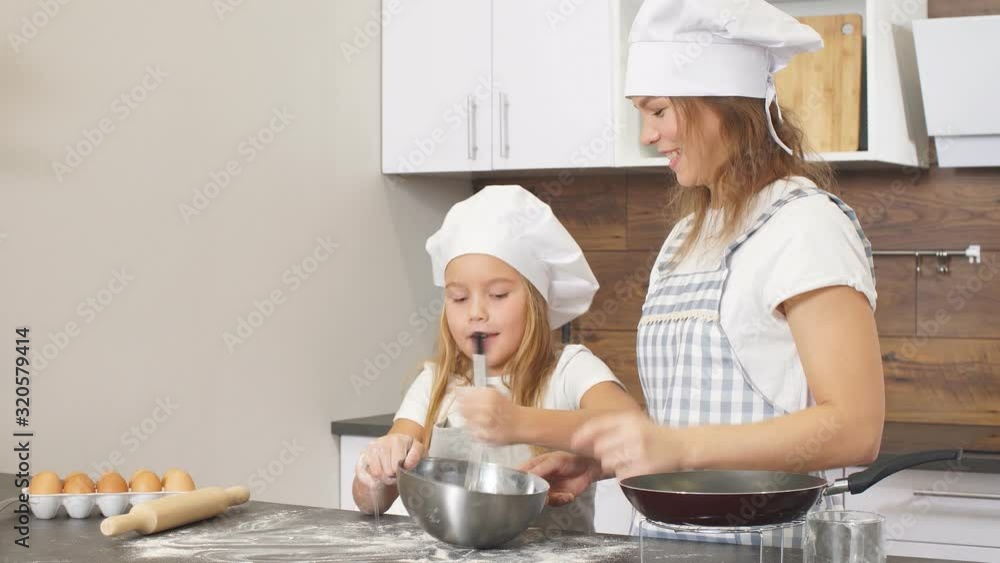 Woman and cute daughter cooking on kitchen, making dough for birthday party.