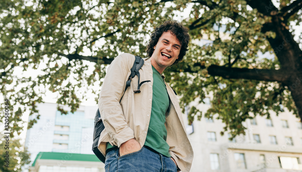 Smiling man with curly hair, posing for social advertisement, posing on the city street. Excited cheerful student male has joyful expression.