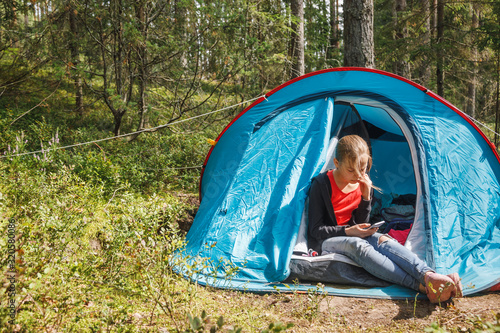 Girl using smartphone sitting in a camping tent during summer holidays