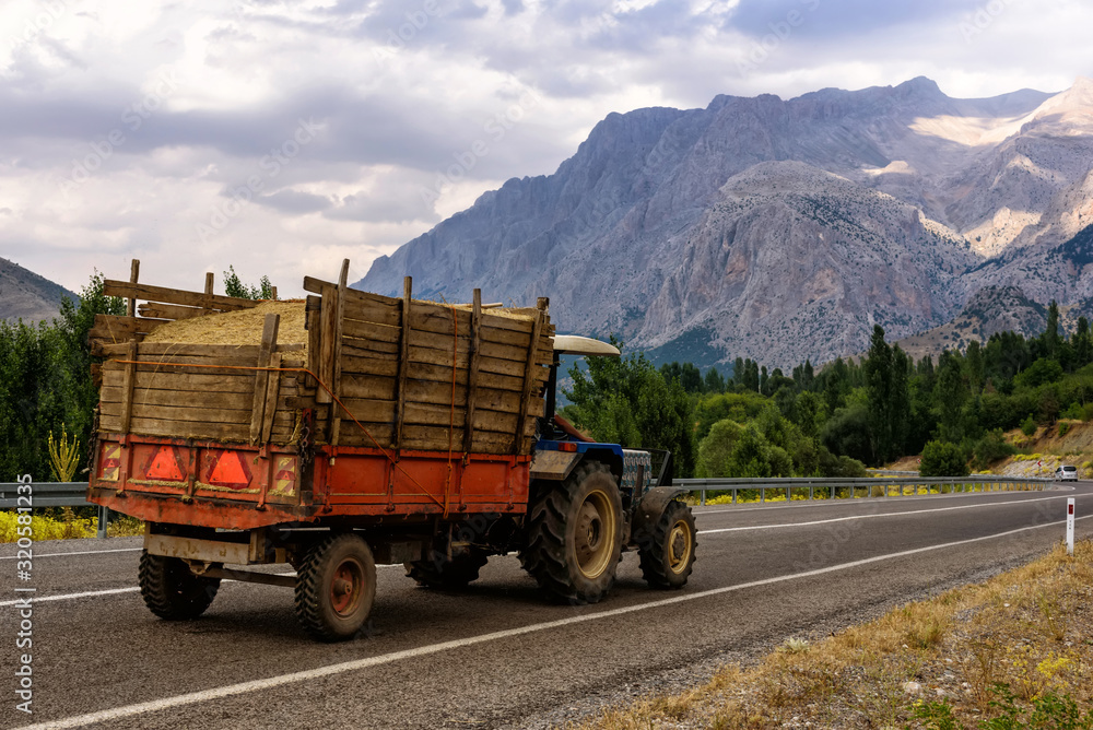 Panoramic view of the mountain with tractor on the road, forest and cloudy sky in summer