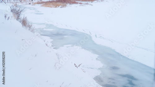 Thin ice melts on the river in early spring. Snowy riverbank with dry grass. Pure and clean nature concept