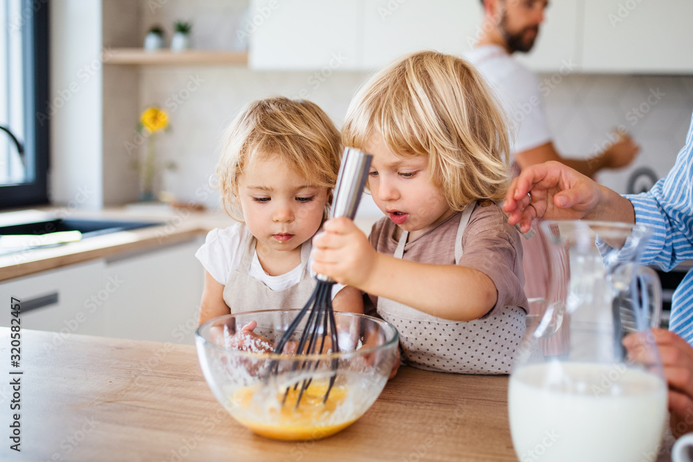 Young family with two small children indoors in kitchen, preparing food. Young family with two small children indoors in kitchen, preparing food.