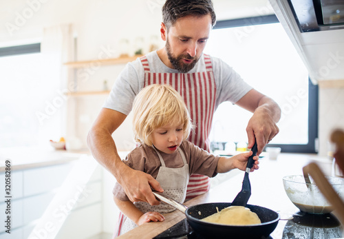 A small boy with father indoors in kitchen making pancakes.