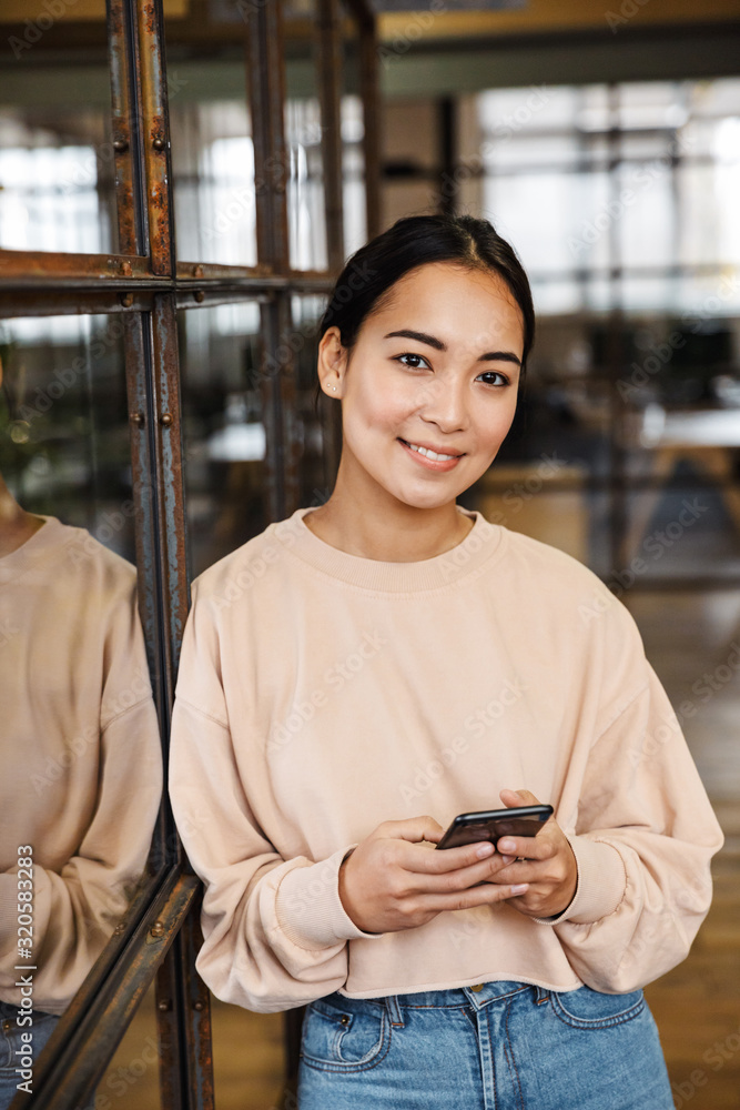 © Drobot Dean - Image of young asian woman holding cellphone while working in office © Drobot Dean - Image of young asian woman holding cellphone while working in office