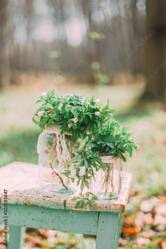 Bouquet of white spring flowers in Glass Jar On wooden chair in the forest outdoors
