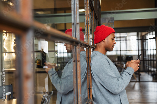 Image of african american man holding cellphone while working in office