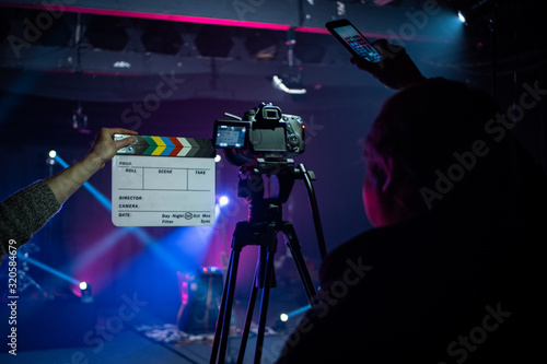 Camera Man or Director operating a Video Camera or DSLR and Clacker board Shooting a music video or concert with stage lighting.  photo