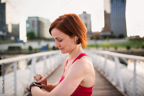 Young woman with smartwatch on bridge outdoors in city, resting after exercise.