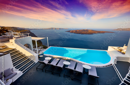 Swimming pool on the hotel terrace of fira's town on Santorini island, Greece. Incredibly romantic sunset on Santorini. Oia village in the morning light. Amazing sunset view with white houses. © zicksvift