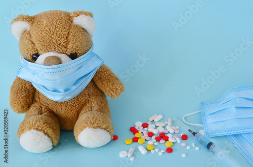 Toy bear in a medical protective mask, a syringe with a vaccine, multi-colored pills on a blue background. Protection, prevention of coronavirus, colds. Concept of illness, cold and flu.copy space.