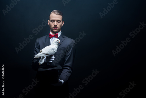 young magician showing trick with dove and hat in dark room with smoke