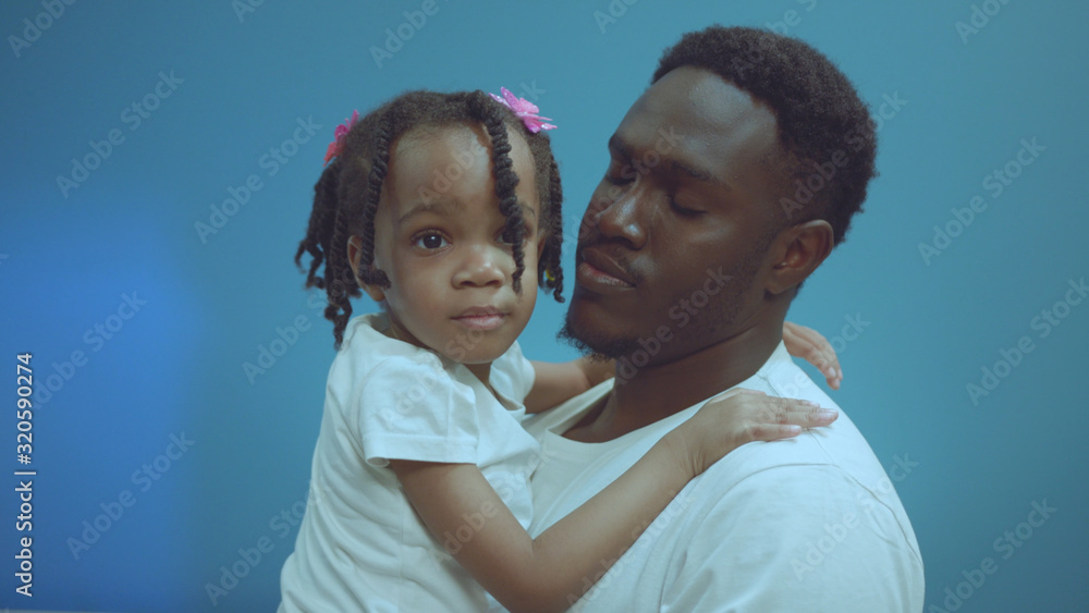 Portrait of cheerful african american dad holding and hugging cute little daughter isolated on blue background. Portrait of cheerful african american dad holding and hugging cute little daughter isolated on blue background.