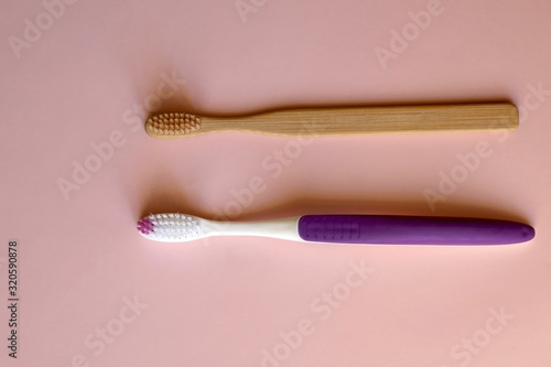 Plastic and bamboo toothbrush on pale pink background. Transition to zero waste lifestyle. Flat lay.