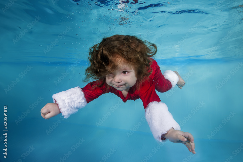 Funny long-haired boy in a Christmas outfit dives underwater in a swimming pool