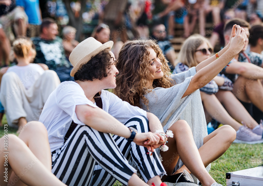 Fototapeta premium Group of young friends sitting on ground at summer festival.