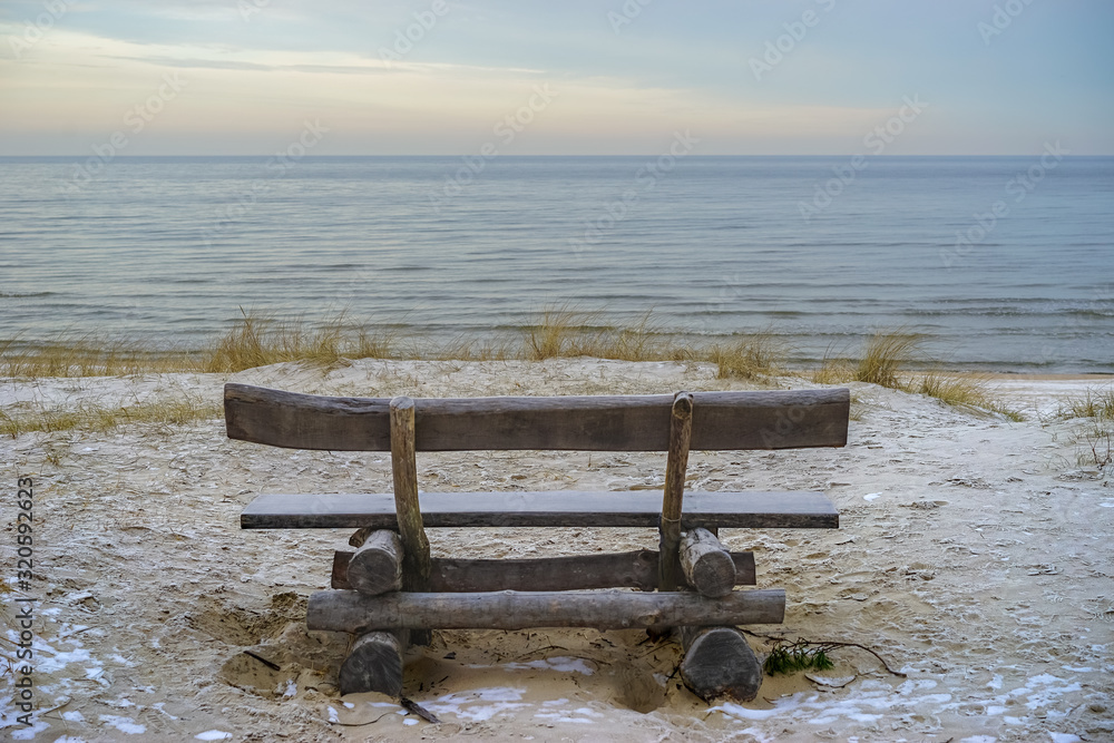 Empty bench made of logs by the Baltic Sea on a sand dune on a cold February morning at sunrise. Relaxation, loneliness, contemplation, outdoor concept. With copy space