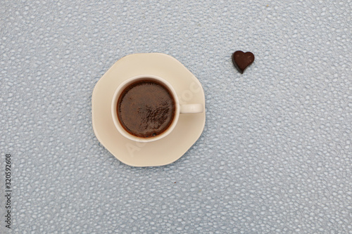 Close-up - a cup of coffee, next to two heart-shaped chocolates.