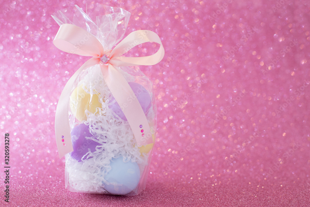 Multi-colored purple, pink, blue, yellow Easter eggs in a transparent gift package, decorated with a bow and rhinestones, on a pink shiny bokeh background. Symbol of celebration of religious holiday Multi-colored purple, pink, blue, yellow Easter eggs in a transparent gift package, decorated with a bow and rhinestones, on a pink shiny bokeh background. Symbol of celebration of religious holiday