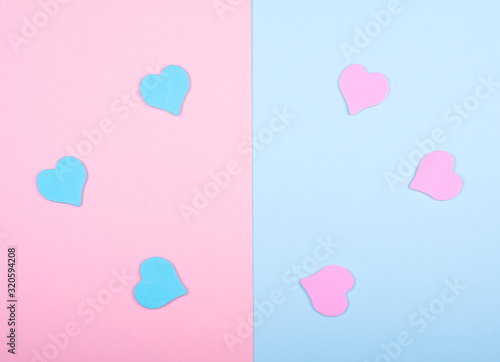 Blue and pink paper hearts on a split pink and blue background (top view, minimalist style)