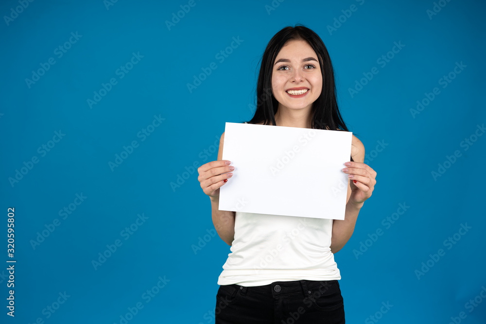 Front view of laughing girl showing blank paper isolated on blue background Front view of laughing girl showing blank paper isolated on blue background