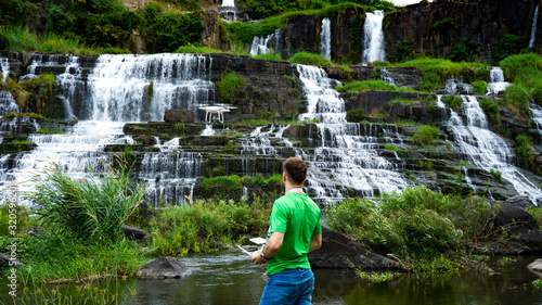 Traveler man controlling drone near the big Da lat waterfall. Drone pilot in beautiful landscape of Pongour waterfall. photo