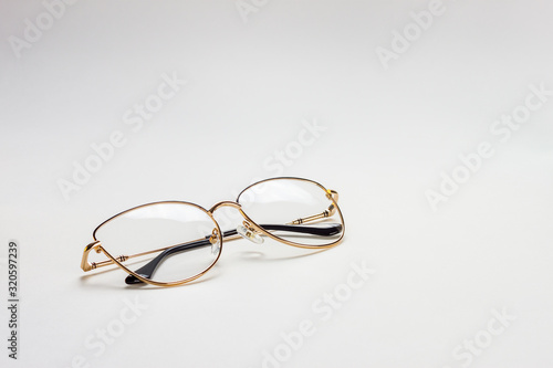 The perspective view of a golden female medical eyeglasses with folded temples on a white background