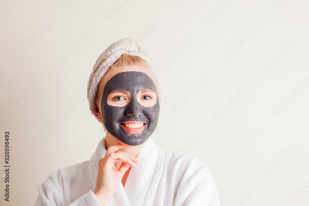 Laughing young girl with a towel on her head using a black mask on her face