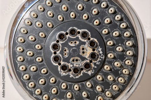 Close-up of an old used silver and grey colored shower head with limescales in the bathroom in front of white tiles