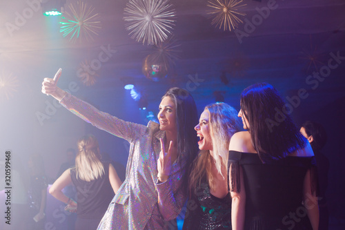 Excited happy women are taking a selfie together in a nightclub using a smart phone