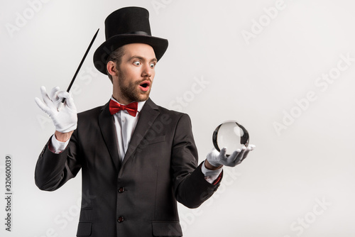 Wallpaper Mural shocked magician holding wand and magic ball, isolated on grey