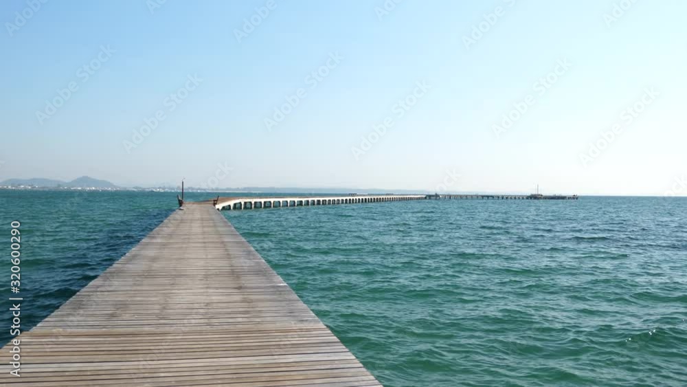 A long pier stretching out into the far horizon in the early morning among gentle blue sea and ripling waves. A long pier stretching out into the far horizon in the early morning among gentle blue sea and ripling waves.