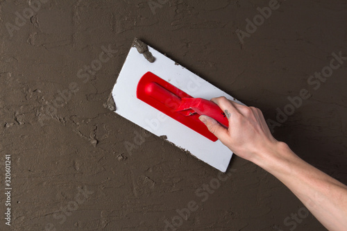 Hand holding a spatula with construction mix and smoothes out bumps.Repair the wall. Plaster the wall with a putty knife.Internal construction and finishing works.The Builder puts plaster on the wall